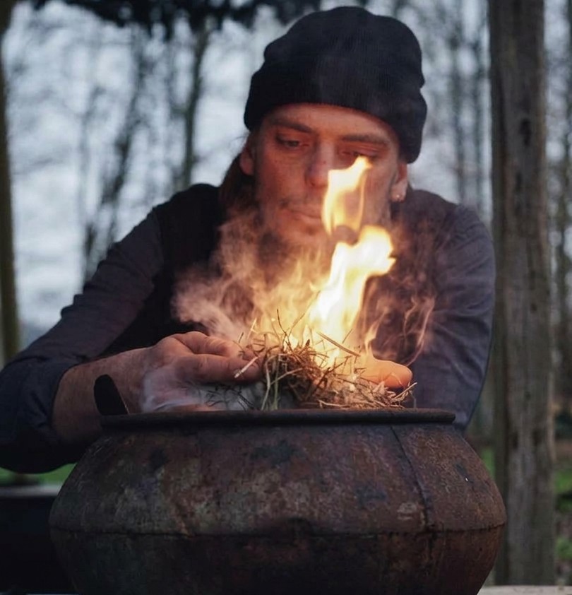 Philipp lighting a fire of dry grass over a cast-iron pot
